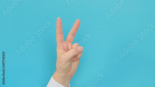 A hand in a white shirt shows the V gesture with two fingers on a blue background. 4k footage photo