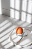 Boiled egg in hard light with window shadows on white kitchen background. Light protein breakfast concept, minimalism, high key