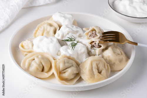 Traditional russian pelmeni, ravioli, dumplings with meat and sour cream in a white plate