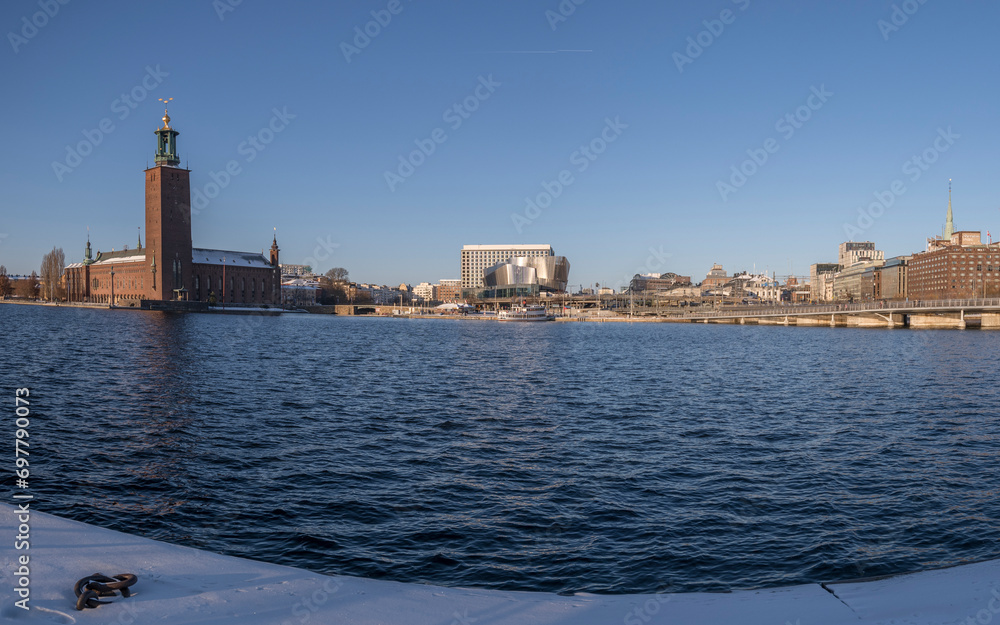 Town city hall and hotels, offices and the Stockholm Waterfront conference building from a snowy pier with mooring ring a snowy sunny winter day in Stockholm