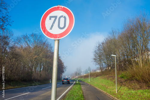 Verkehrsschild 70 km an Einfahrtsstrasse an Ortseingang mit Fahrradweg vor blauem Himmel