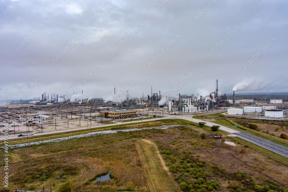 Aerial view of a Fuel Refinery in Port Arthur Texas with fuel storage, pipelines, steam rising from tall chimneys and an overcast sky above.