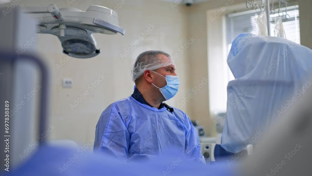 Cropped view of a surgeon working at surgery. Doctor in cap and mask looks aside at the screen watching the operation progress. Cropped view of a surgeon working at surgery. Doctor in cap and mask looks aside at the screen watching the operation progress.