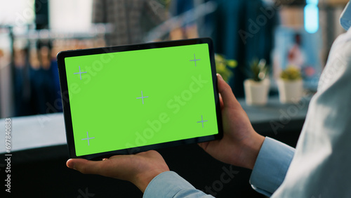 Boutique worker analyzing digital device with chroma key green screen mock up display, working in clothing store. Asian worker holding tablet computer in shopping mall. Technology concept