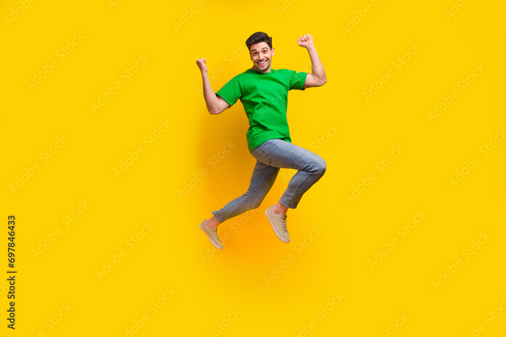 Full length photo of ecstatic satisfied man dressed green t-shirt flying raising fists up win betting isolated on yellow color background