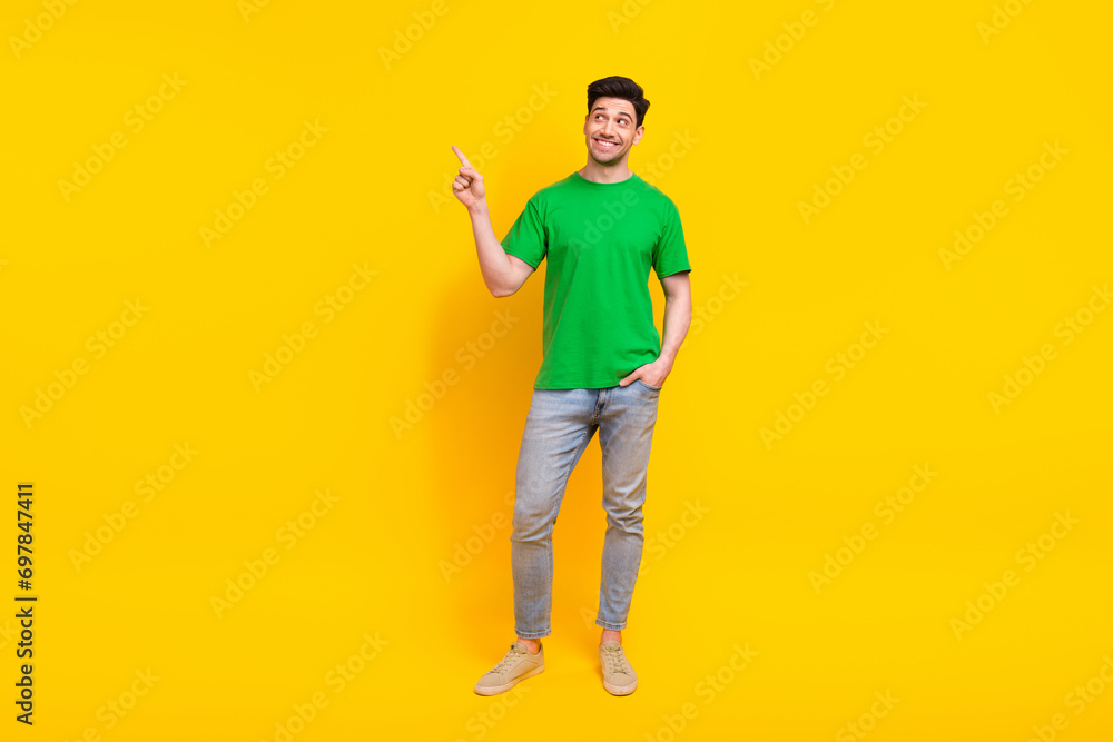 Fototapeta premium Full length photo of positive man dressed green t-shirt jeans look directing at sale empty space isolated on yellow color background