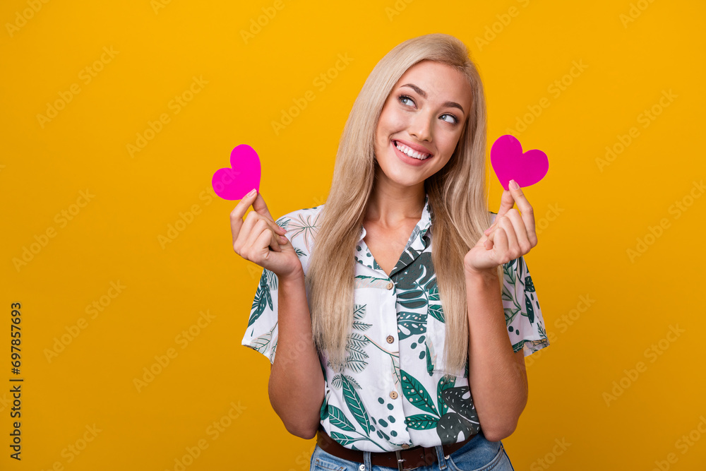 Portrait of gorgeous cute girl wear flower print blouse holding paper hearts look at promo empty space isolated on yellow color background