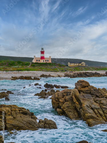 Cape Agulhas Lighthouse, southernmost tip of Africa from the ocean with rocks and blue water, L'Agulhas, South Africa