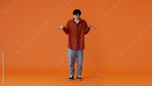 Confused asian man shrugging and feeling awkward in studio photo