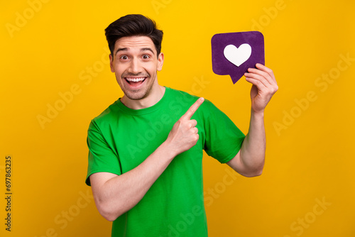 Photo portrait of nice young brunet male point heart icon notification dressed stylish green garment isolated on yellow color background