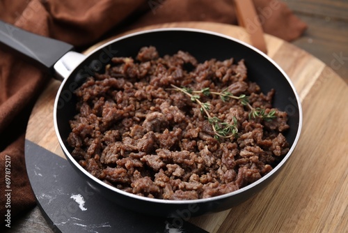 Fried ground meat and thyme in frying pan on wooden table, closeup