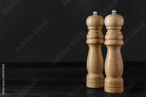 Salt and pepper shakers on black wooden table, closeup. Space for text
