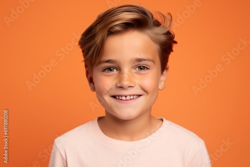 smiling little boy in casual clothes looking at camera over orange background