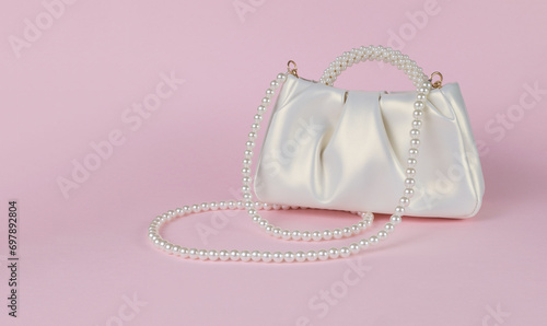 Stylish white women's bag trimmed with pearls on a pink background.