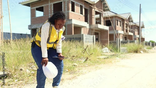 African American female worker inspects construction site working outdoors in excessive heat causing fatigue thirst fainting and discomfort.