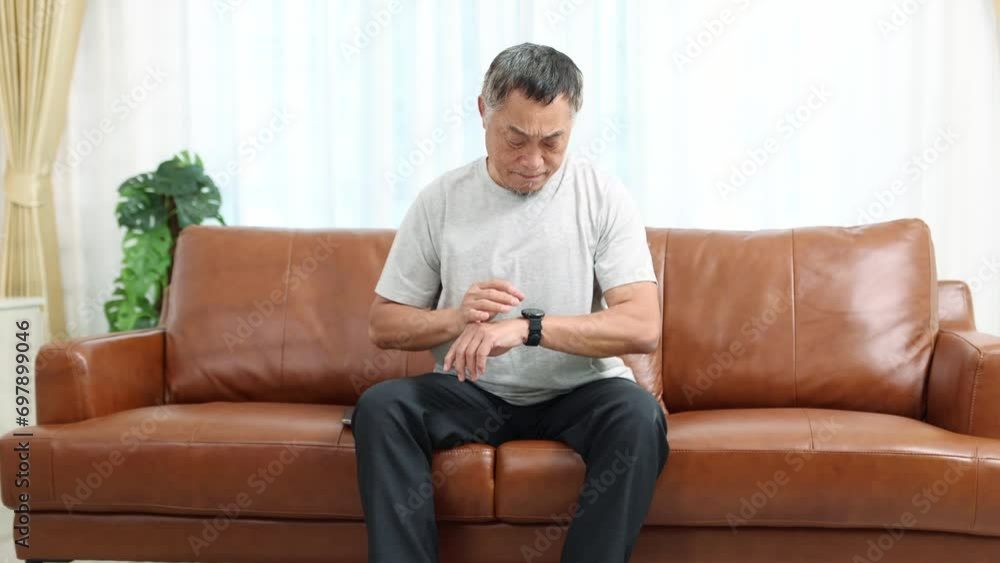 Elderly Asian man with heart problems felt sudden heart muscle pain and was easily tired while sitting on the sofa and trying to measure his heartbeat with wristwatch. Elderly Asian man with heart problems felt sudden heart muscle pain and was easily tired while sitting on the sofa and trying to measure his heartbeat with wristwatch.