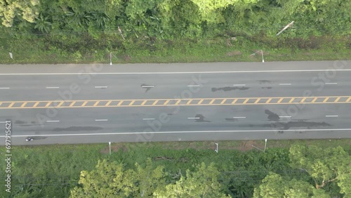 The video shows a drone slowly flying from right to left, capturing a wide road with cars driving smoothly while surrounded by lush forests.
