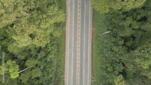 The video shows a drone slowly flying from bottom to top, capturing a wide road with cars driving smoothly while surrounded by lush forests.4k