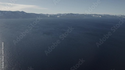 A high-flying, 4K drone shot over Lake Tahoe, California, during the winter season. The camera slowly pans up, revealing the snow-covered Sierra Nevada mountains in the distance, surrounding the lake. photo