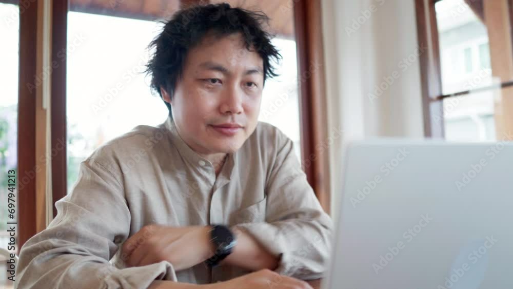 Asian man looking at silver laptop computer in the cafe during daytime Asian man looking at silver laptop computer in the cafe during daytime