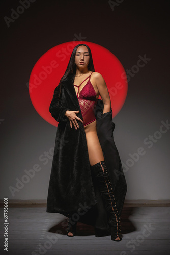 Beautiful asian girl in lingerie and fur coat posing on the gray background in the red lights. Beauty and fashion. photo