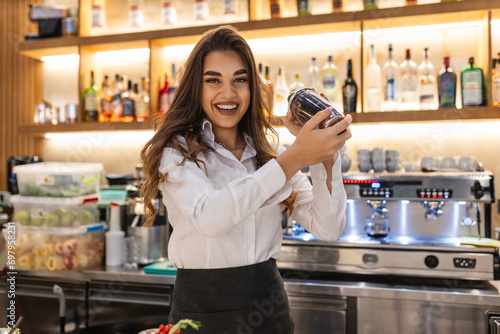 Young female worker at bartender desk in restaurant bar preparing cocktails with shaker. Beautiful young woman behind bar photo