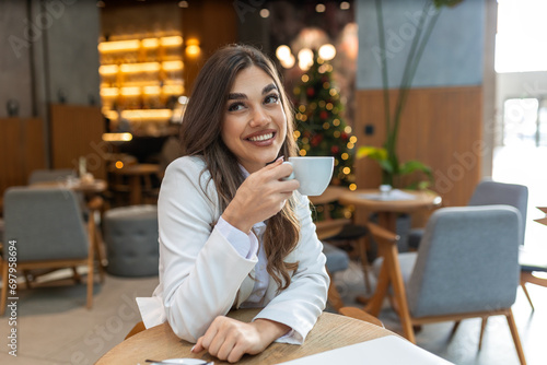 Young beautiful stylish woman in white blazer with cup of coffee. Smiling woman having coffee tea hot beverage sitting in cafe after shopping, relaxing resting alone.