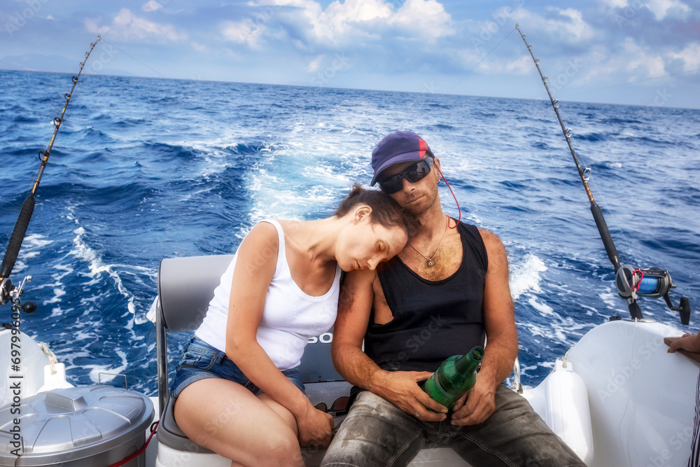 A man in a baseball cap and a girl in a white T-shirt sleep aboard a boat while trolling