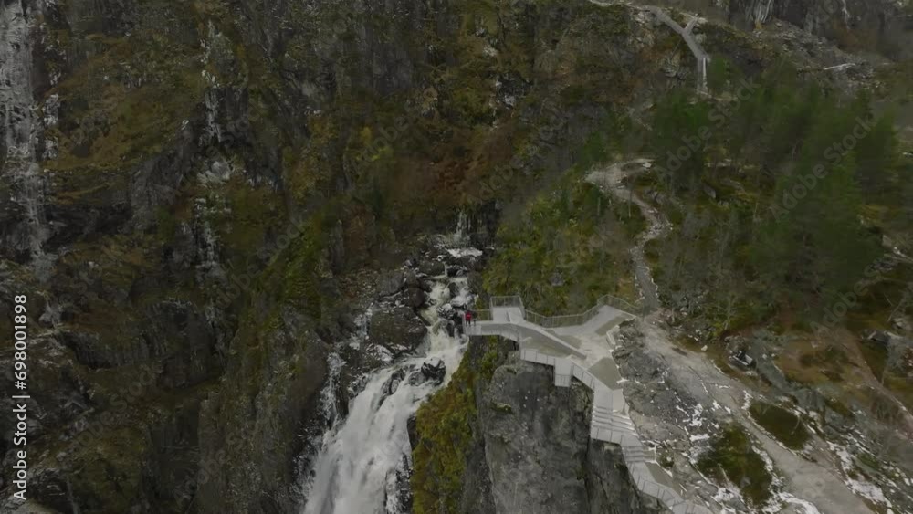 aerial view of a couple stanind at viewpoint at voringfossen waterfall with drone distancing away in norway