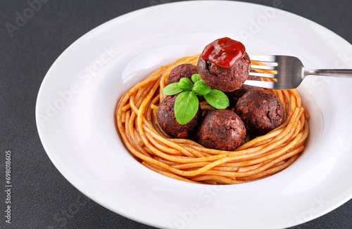 Fried vegan meatballs with noodles and basil leaves on a plate. Fork with a meatball and ketchup.