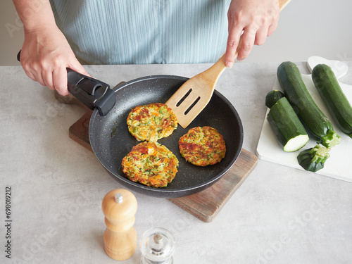 Vegetable pancakes in frying pan held by woman's hands with wooden spatula on the kitchen table. Healthy meal.