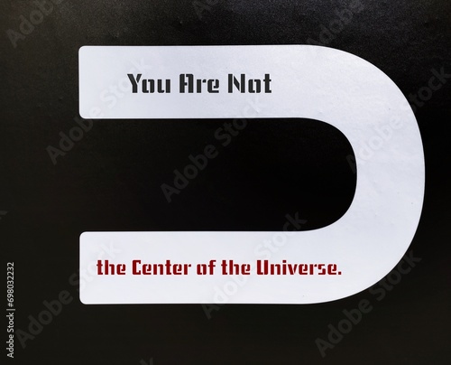 Black wall with U letter and text inscription YOU ARE NOT THE CENTER OF THE UNIVERSE, to remind we are not focus of everyone attention, we are much more focus of ourselves mistakes and flaws
