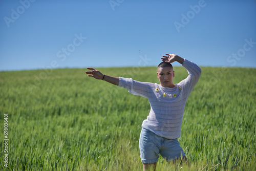 Young  South American  non-binary person  heavily makeup  posing in a white sweater with natural daisies  in the middle of a green wheat field  arms raised. Concept queen  lgbtq   pride  queer.