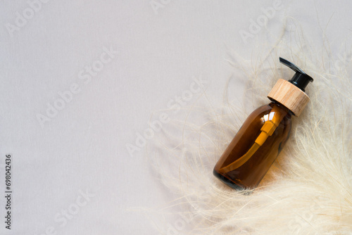 Hair care spa products concept. Cosmetic skin or hair care products with dry flowers on pastel gray background. Brown glass pump bottle. Empty label for product mockup. Flat lay, copy space.