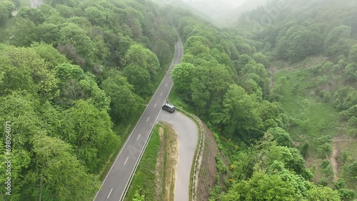 Ascending drone footage of a car driving on the Castle Road on a foggy day in Bourscheid, Luxembourg photo