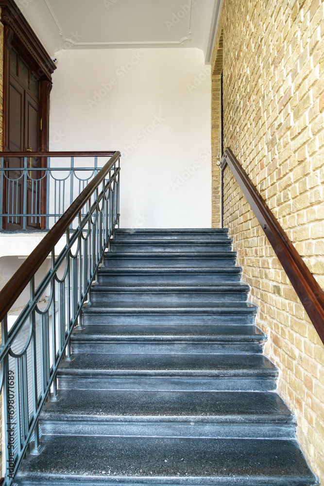 An old antique staircase in a historic building. An empty staircase and brick walls. Cast iron railings framed by wood. An old antique staircase in a historic building. An empty staircase and brick walls. Cast iron railings framed by wood.