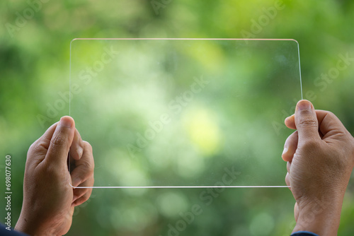 Hand holding and showing transparent tablet device. Business, natural green bokeh background,technology concept,alternative energy,conservative clean energy .