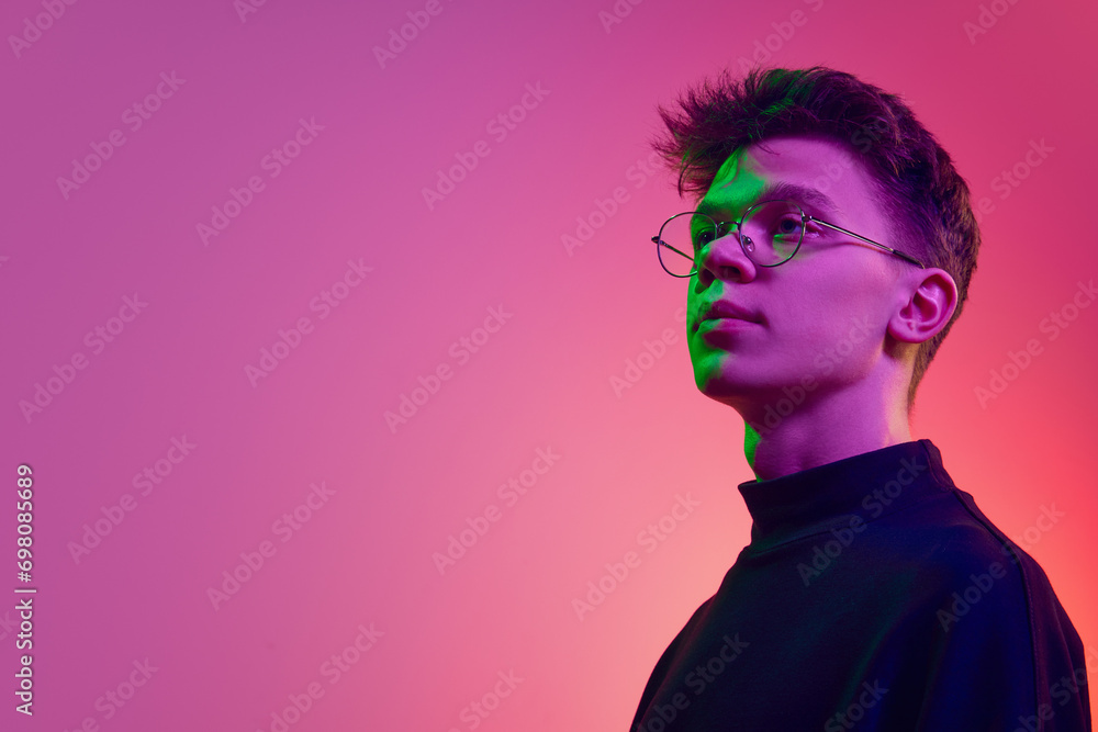 Portrait of young man, student in stylish clothes and glasses standing with proud face against gradient pink background in neon light. Concept of human emotions, youth, growth, achievement