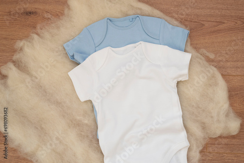 Mockup of white and blue baby bodysuit on wood background. Blank baby clothes template mock up. Flat lay styled stock photo.
