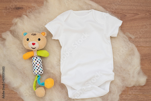 Mockup of white baby bodysuit on wood background. Blank baby clothes template mock up. Flat lay styled stock photo.