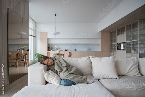 Frustrated young woman lying on couch at home suffering from heartbreaking divorce. Girl feeling bad, apathy hiding from society in loneliness solitude. Mental disorder, anhedonia, stress, sleepiness. photo