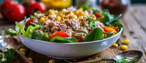 White bowl holds tuna salad with lettuce, tomatoes, carrot, and corn. photo