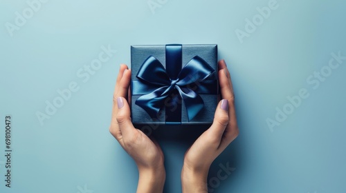 Top view to young woman hands holding navy blue present gift giftbox with satin ribbon bow on light blue background. Christmas, birthday, anniversary, shopping, blue friday concept  photo