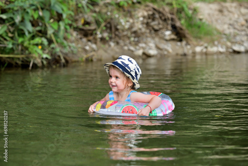 Obraz na płótnie A little girl learns to swim in a river using a lifebuoy w salonie