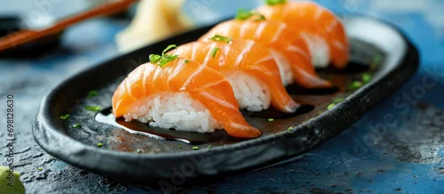 Obraz  z motywem Close-up vertical macro shot of sushi salmon on a black plate on a blue concrete table.