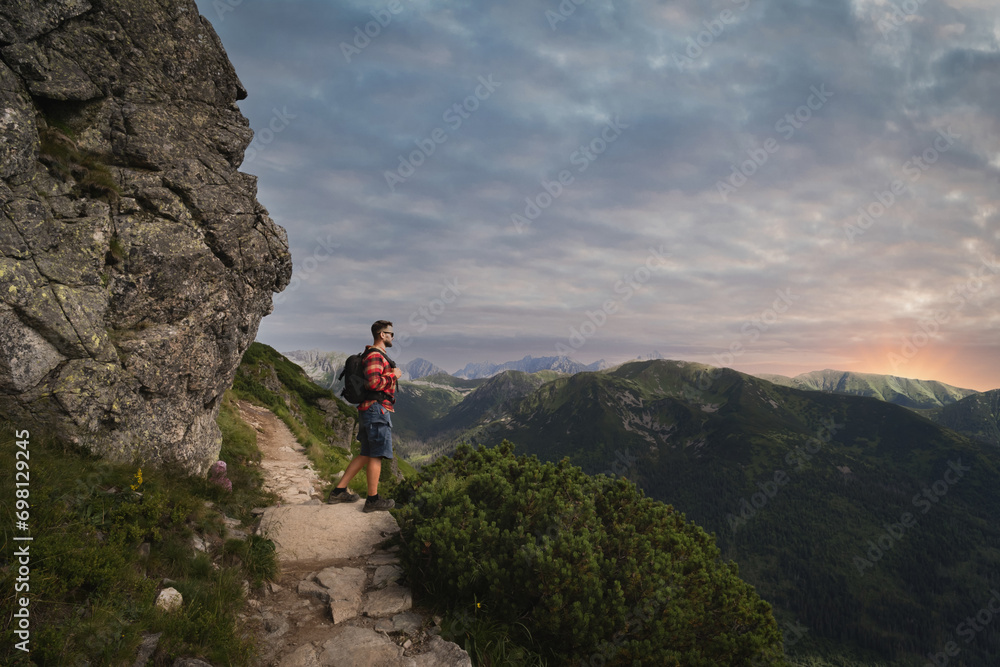 A male traveler with a briefcase on his back on a hike in the Polish Tatra Mountains at sunset.