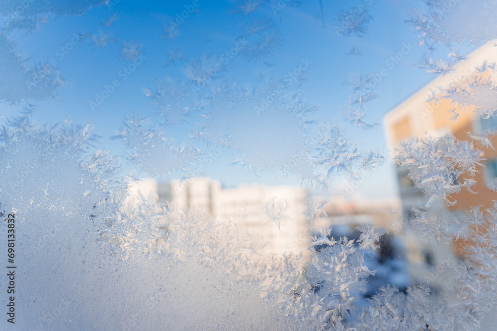 Frozen snowflakes on the window, frost drawing its patterns on the glass, cold season, winter outside the window.