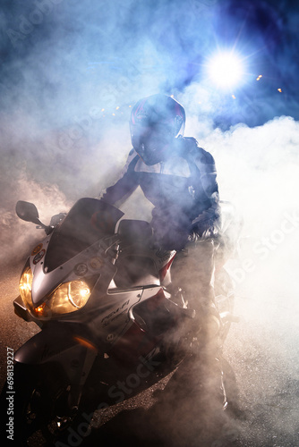 Motorcyclist in a leather jacket suit through the red and blue smoke on a motorcycle at night