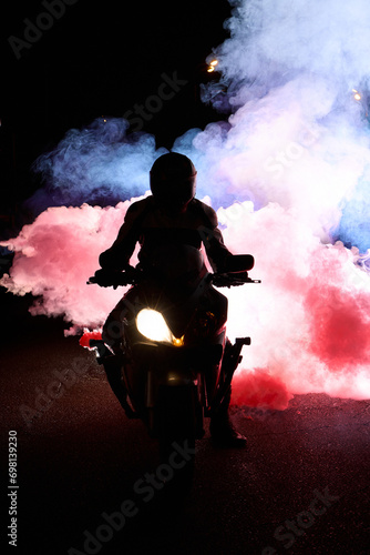 Motorcyclist in a leather jacket suit through the red and blue smoke on a motorcycle at night