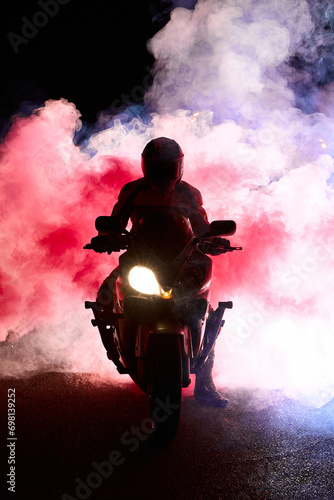 Motorcyclist in a leather jacket suit through the red and blue smoke on a motorcycle at night